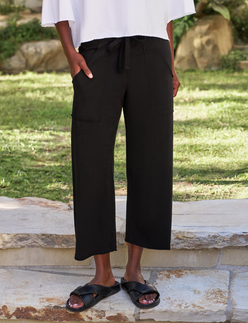 Person wearing black wide-leg pants and black sandals standing on a stone surface with grass in the background., front view