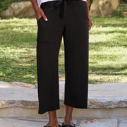 Person wearing black wide-leg pants and black sandals standing on a stone surface with grass in the background.
