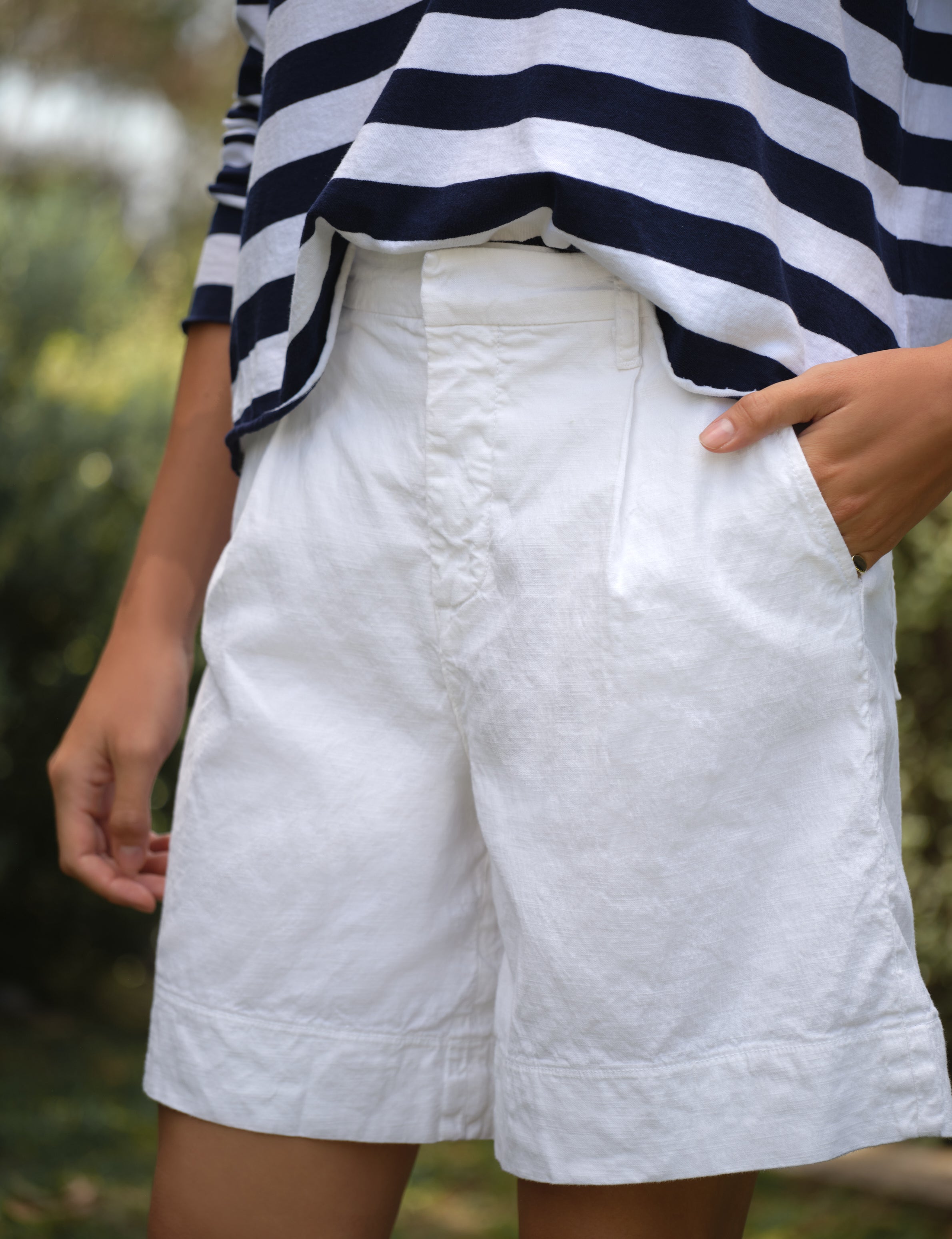 Person wearing a striped shirt and white shorts with a blurred natural background, view 3