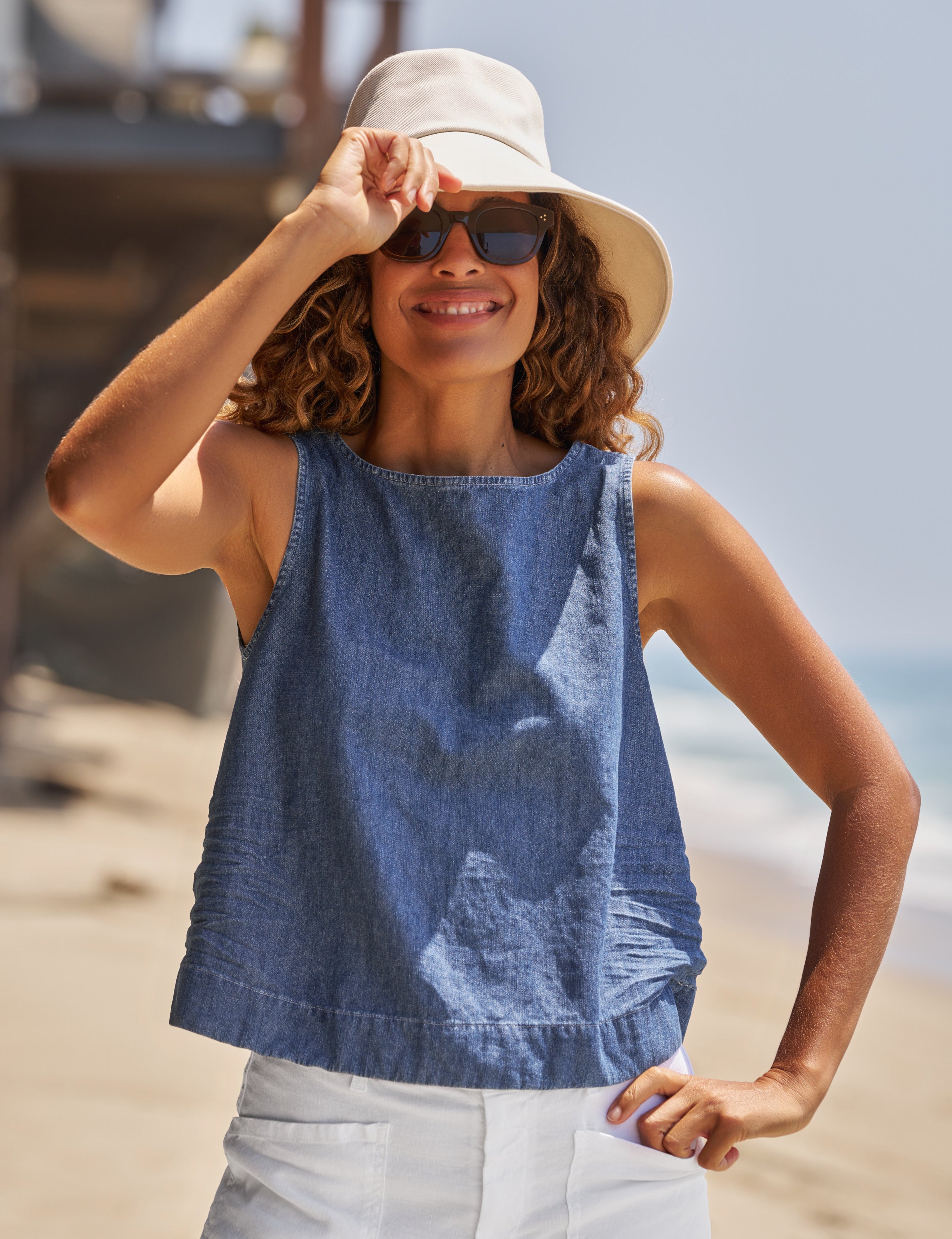 Woman wearing a blue sleeveless top and beige hat on a beach., front view
