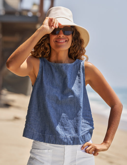 Woman wearing a blue sleeveless top and beige hat on a beach., front view