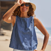 Woman wearing a blue sleeveless top and beige hat on a beach.