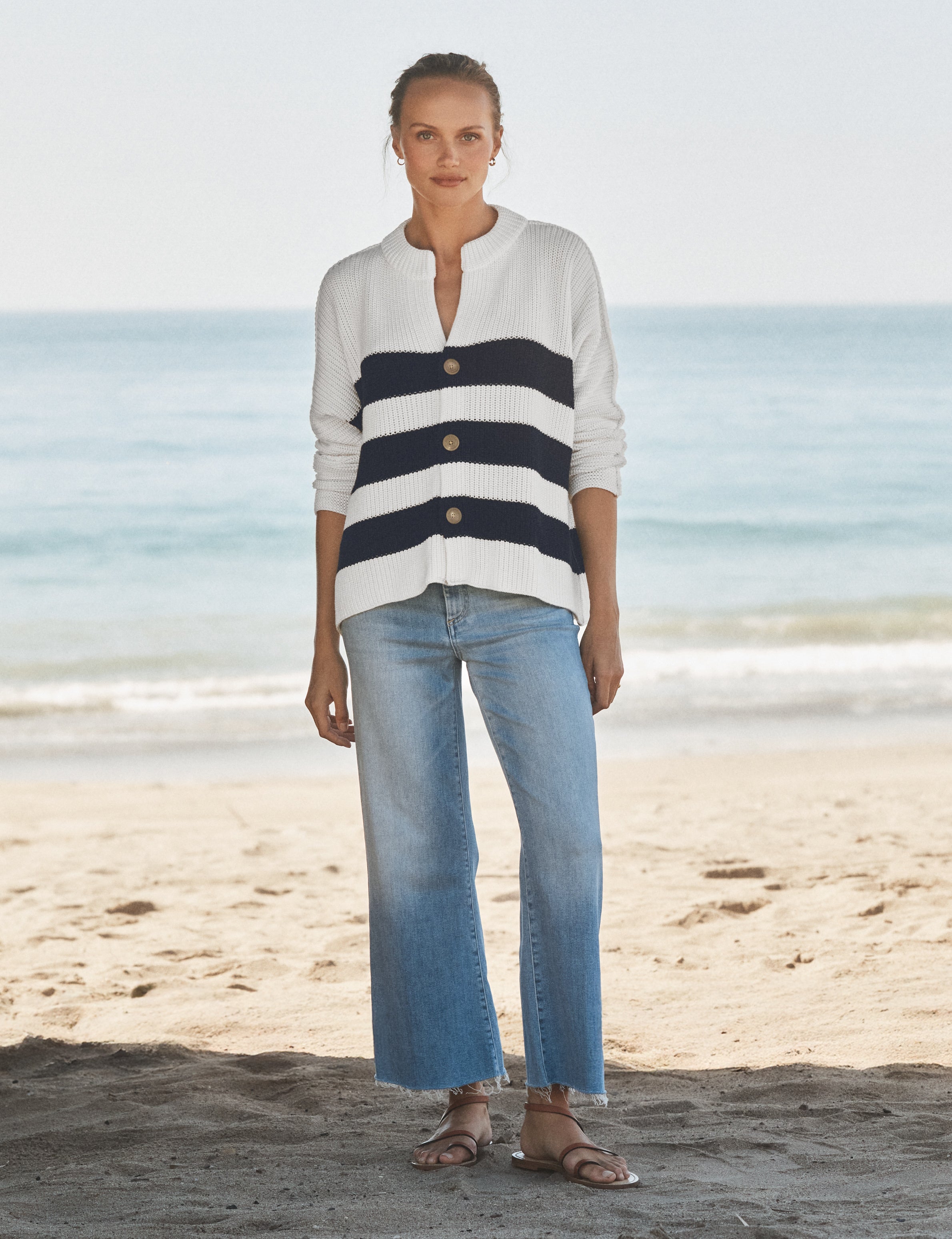 Woman wearing a striped shirt and jeans standing on a beach., view 4