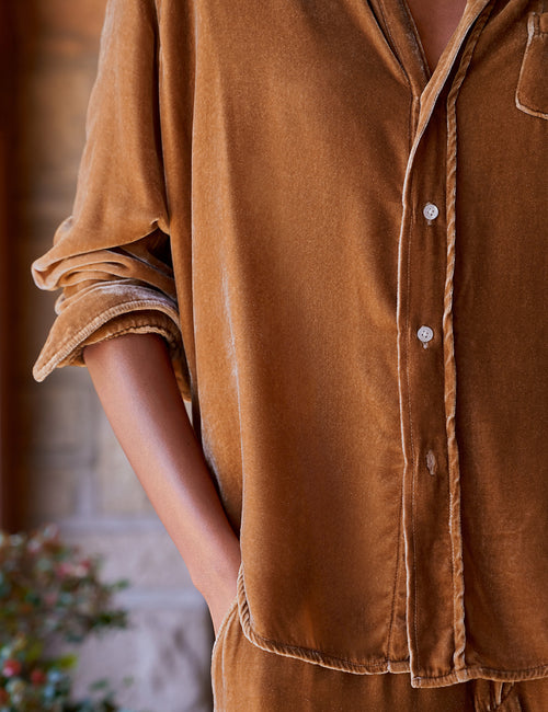 A close-up of a person wearing a warm gold velvet button-up shirt with rolled sleeves and a matching pair of pants, shown in an outdoor setting., view 3