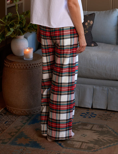 A woman stands in a living room wearing a white short-sleeve t-shirt and red, black, and white plaid pants, viewed from behind., alternate view