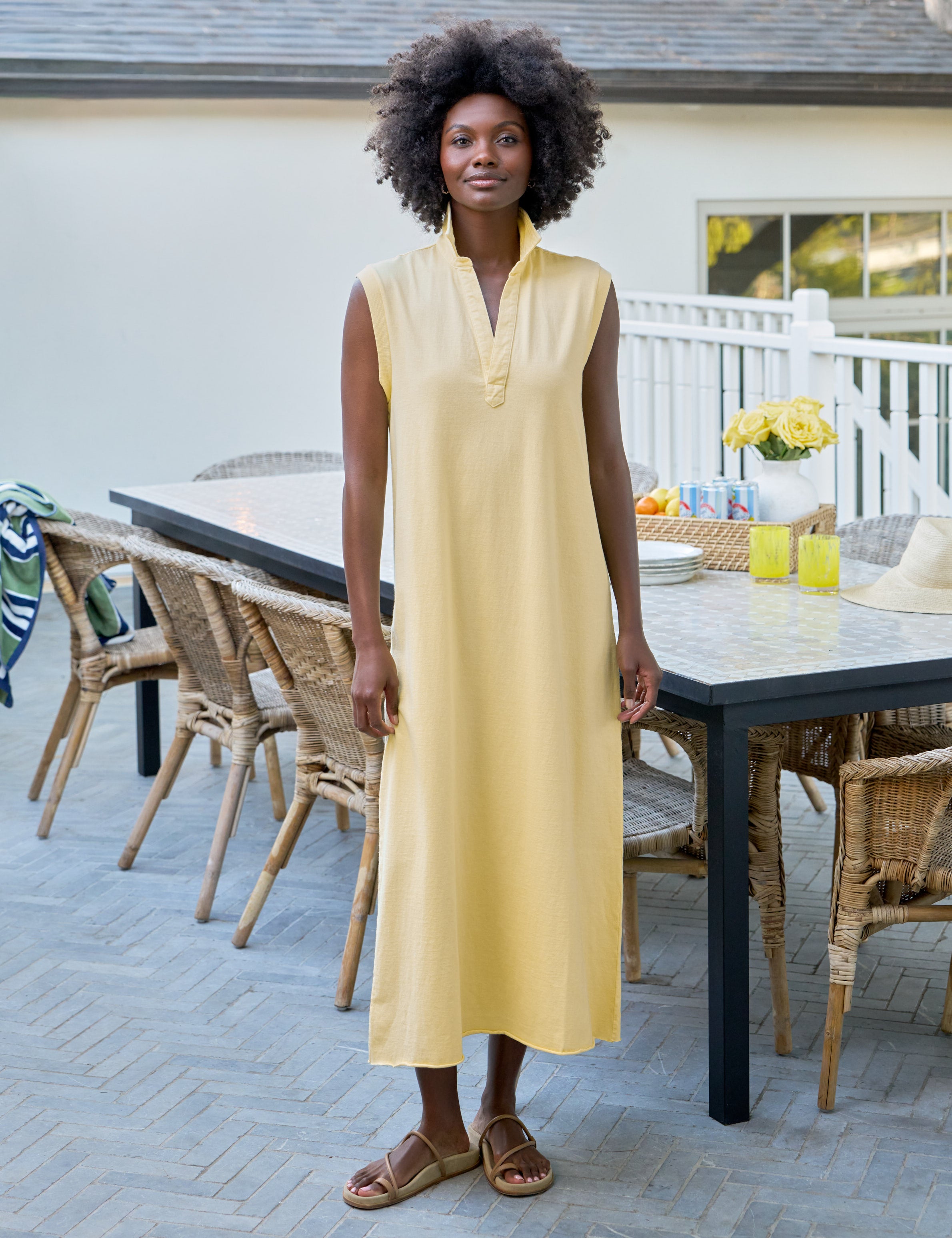 Woman in a yellow dress standing outdoors near a dining table with chairs.