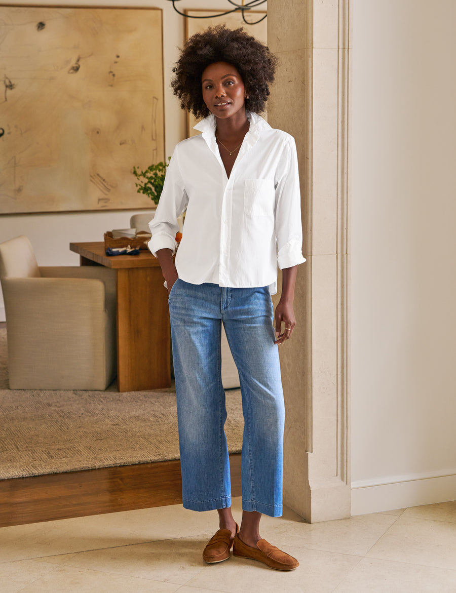 Woman wearing a white shirt and blue jeans standing in a living room.