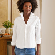 Woman wearing a white shirt and blue jeans standing in a room with a wooden desk and plants.