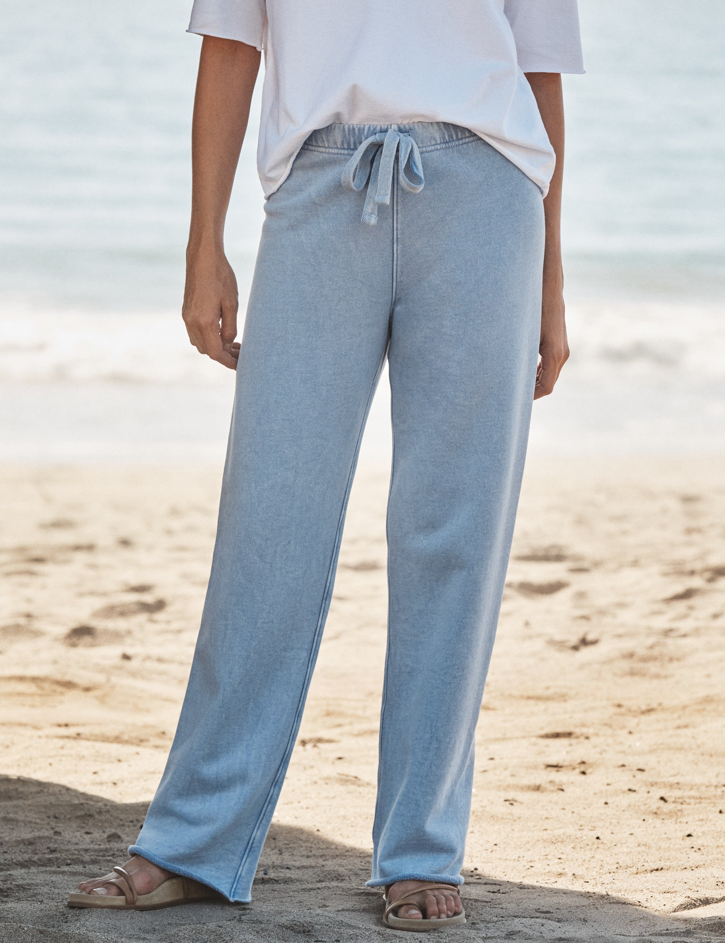 Person wearing light blue pants and a white top on a beach., front view