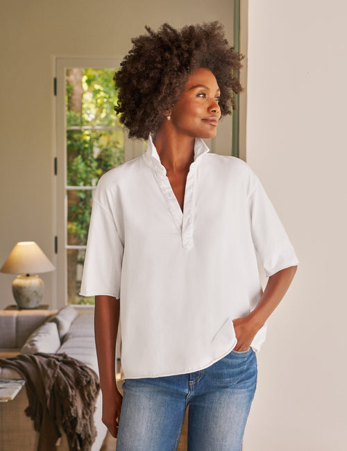 Woman wearing a white shirt and blue jeans standing in a room with a couch and lamp., front view