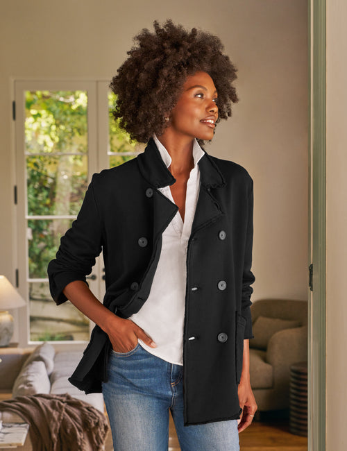 Woman wearing a black coat over a white shirt and blue jeans in a living room., front view