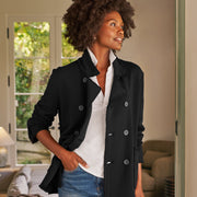 Woman wearing a black coat over a white shirt and blue jeans in a living room.
