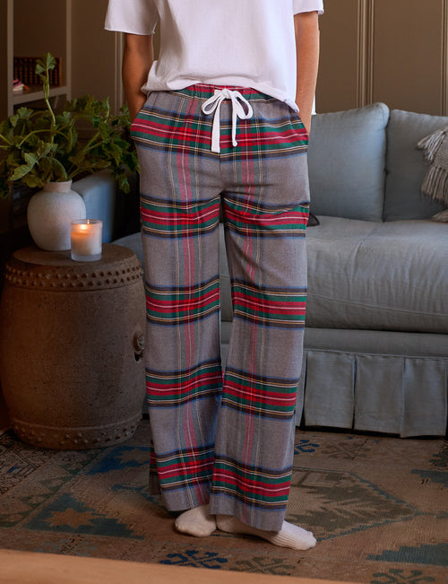 A woman stands in a cozy living room wearing a white short-sleeve t-shirt and gray plaid lounge pants with red, green, and blue stripes, white drawstrings, and white socks., front view