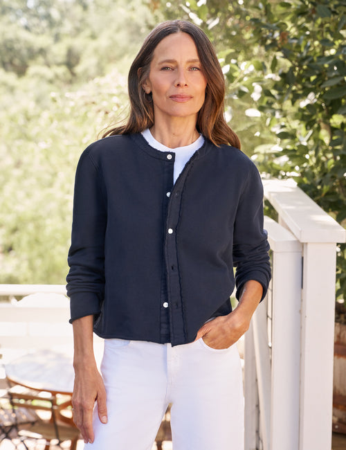 Woman wearing a navy cardigan over a white shirt and pants, standing outdoors with greenery in the background., front view