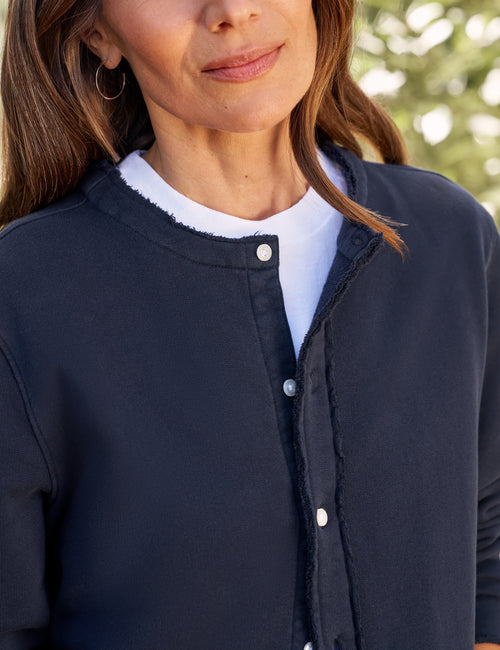 Person wearing a navy blue jacket with a blurred green background, view 3