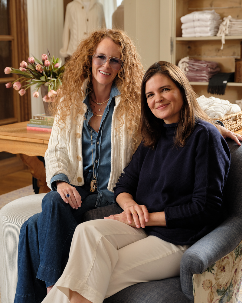Two women sitting on a couch in a store setting with shelves and products in the background.