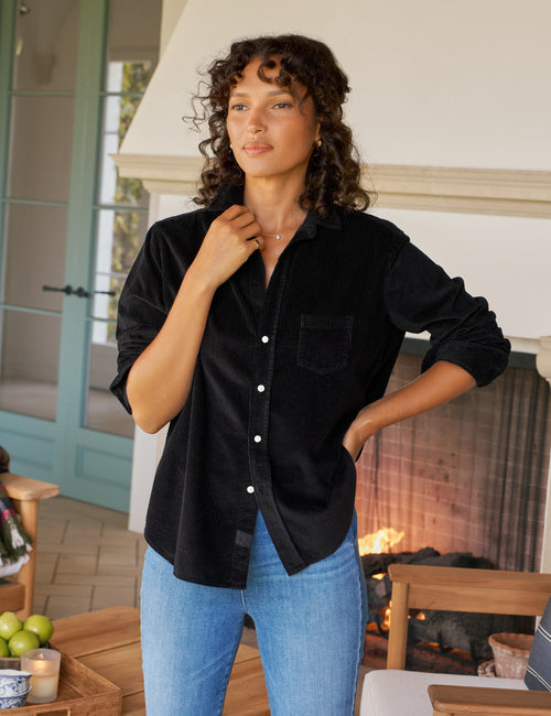 Woman wearing a black shirt and blue jeans standing in a cozy indoor setting., front view