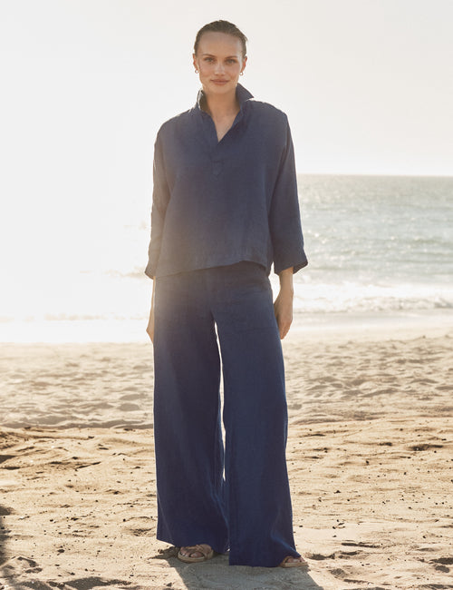 Woman in a blue outfit standing on a beach with ocean in the background, front view