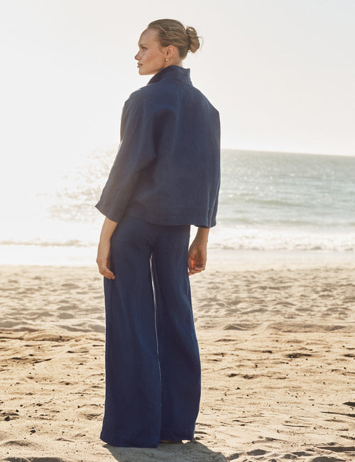 Woman in a navy outfit standing on a beach with ocean in the background, alternate view