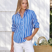 Woman wearing a blue and white striped shirt with white pants, standing against a white wooden fence.