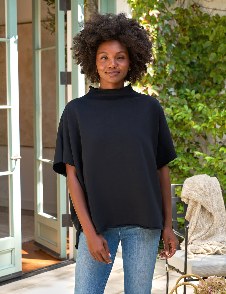 Woman wearing a navy top and blue jeans standing outdoors.