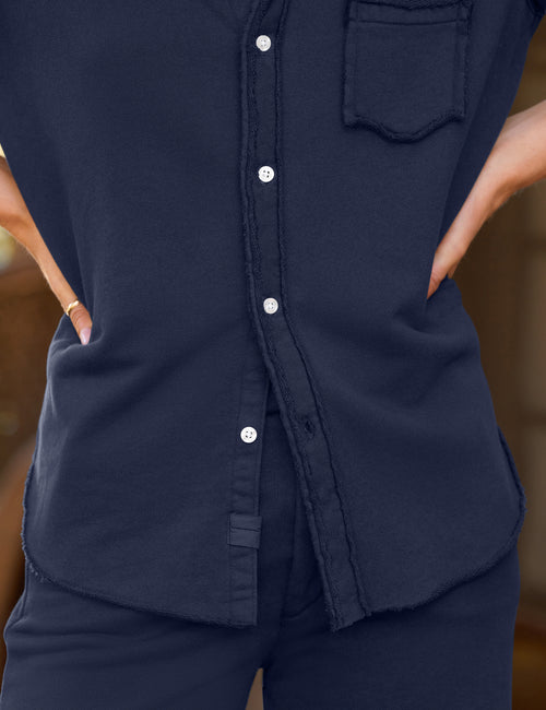 Close-up of a person wearing a dark navy button-front top with a chest pocket and side pockets, paired with matching navy bottoms. The photo is cropped from the shoulders to the hips, with hands in the pockets., view 3