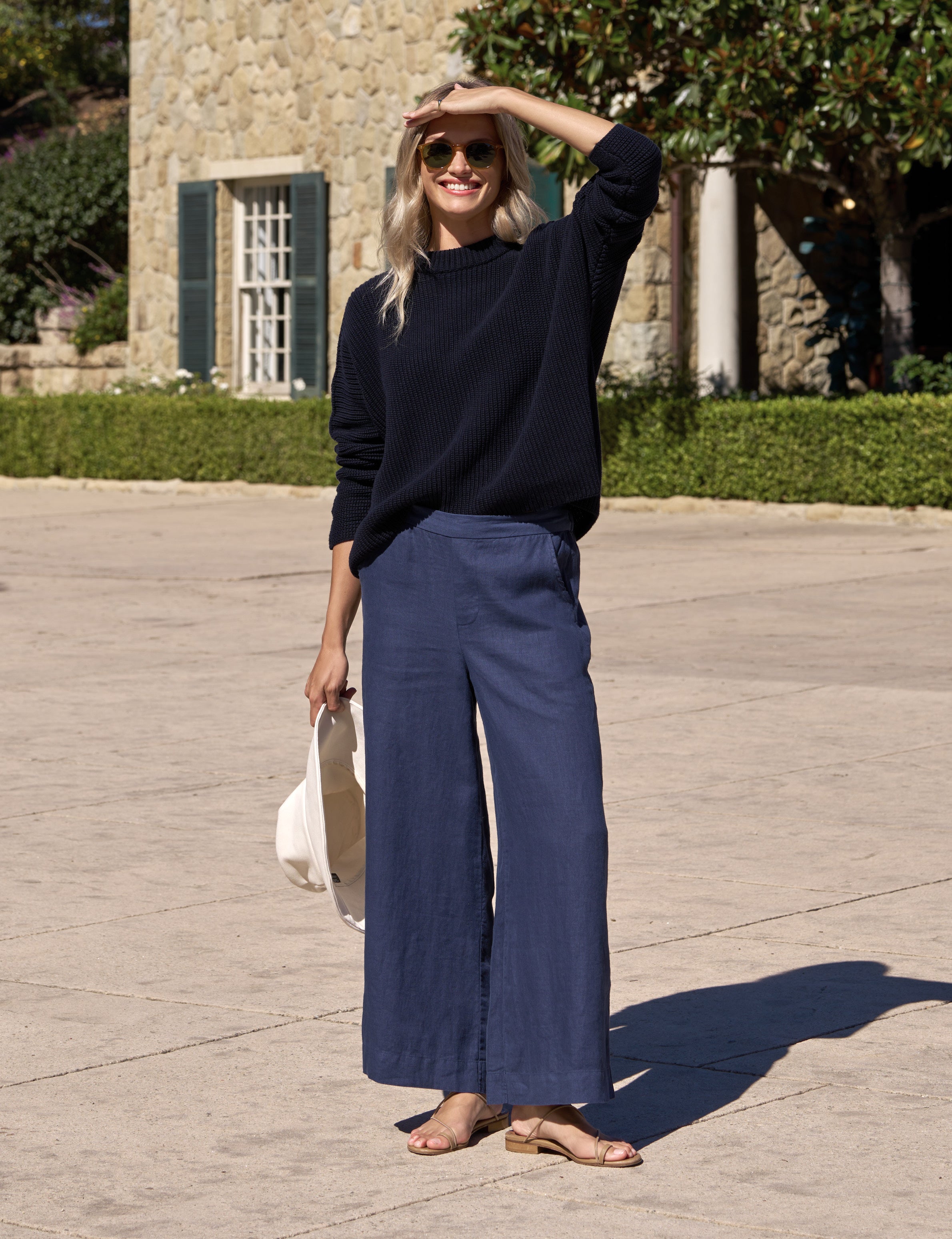 Woman in navy sweater and wide-leg pants standing outdoors on a stone path.