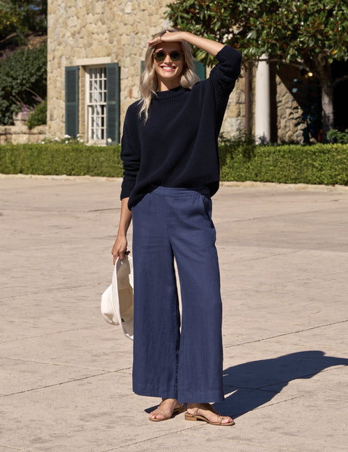 Woman in navy sweater and wide-leg pants standing outdoors on a stone path., view 5