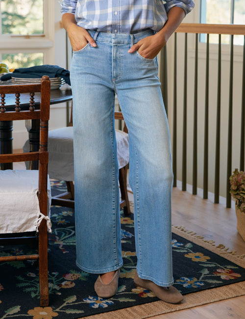 Person wearing light blue jeans and a plaid shirt in a home setting., front view