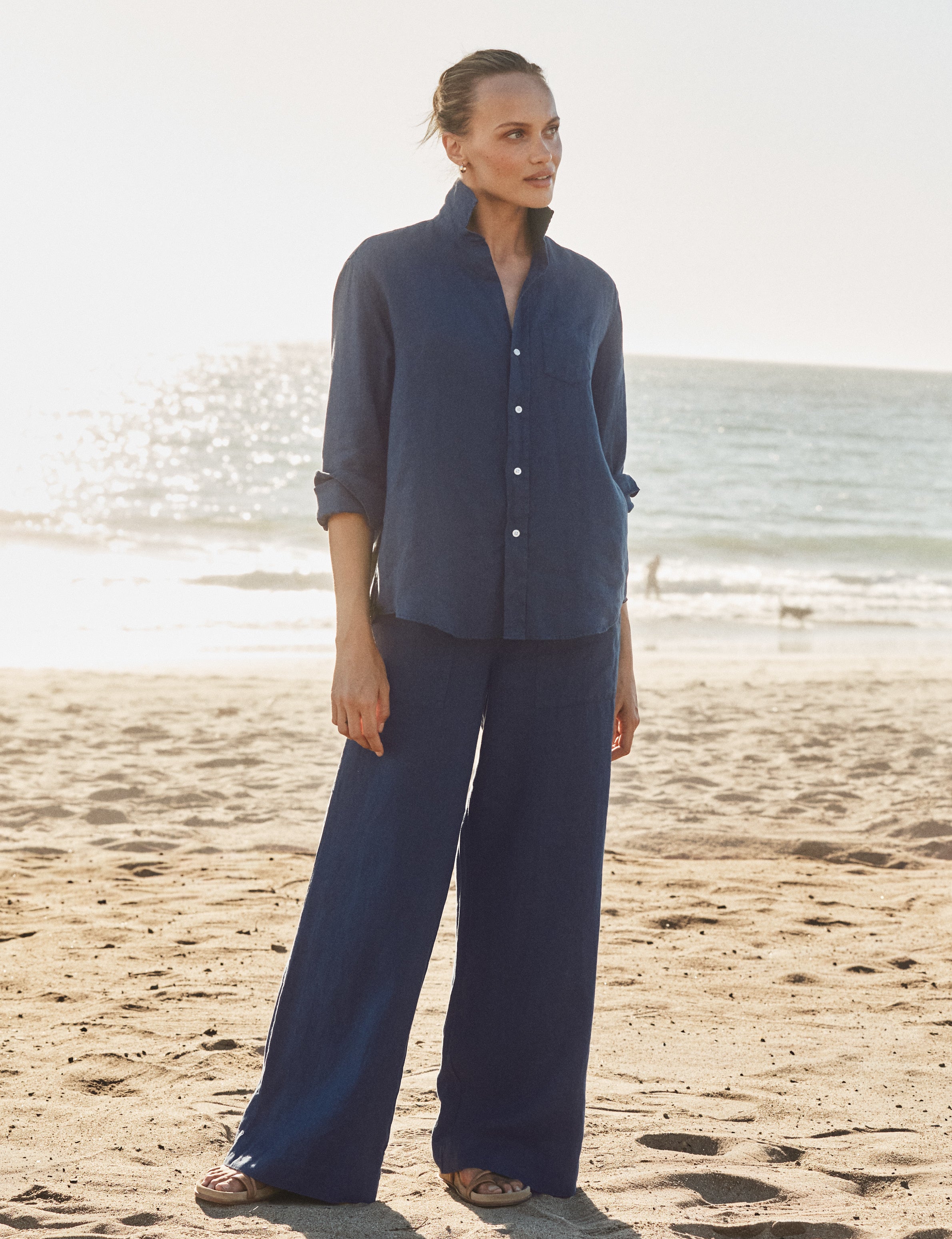 Woman in a navy outfit standing on a beach with ocean in the background, front view