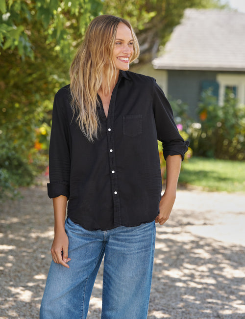 Woman wearing a black shirt and blue jeans standing outdoors., alternate view