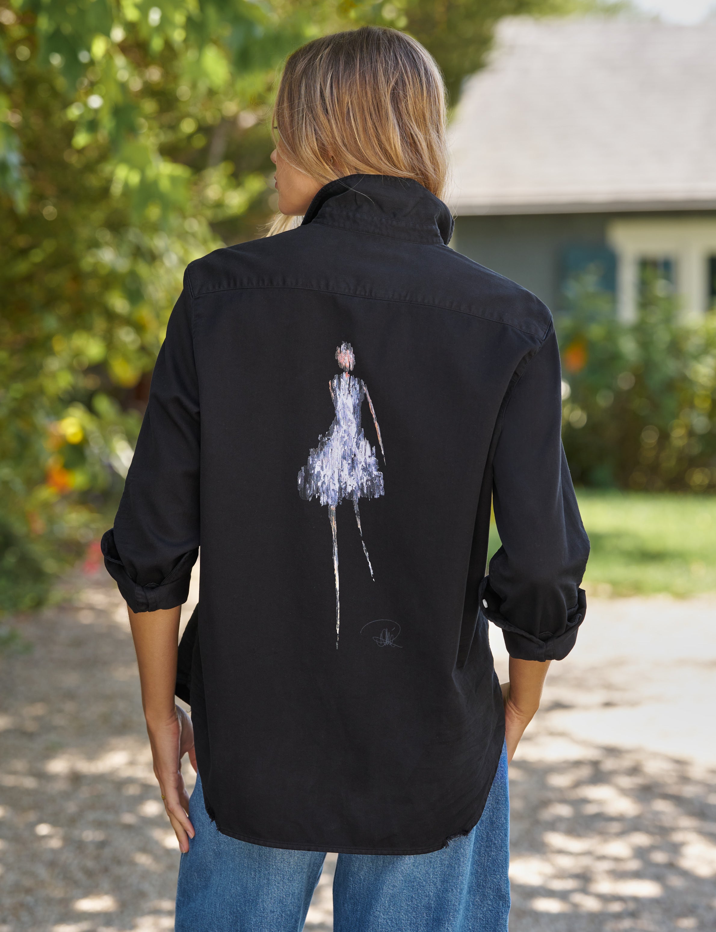 Person wearing a black shirt with a white graphic on the back, standing outdoors., front view