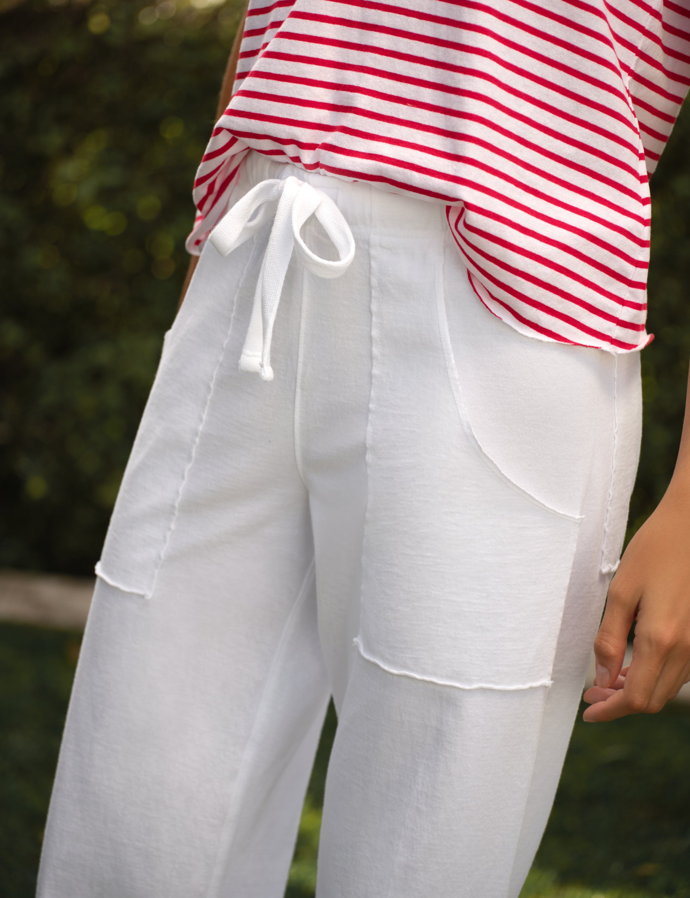 Person wearing a red and white striped shirt with white pants in a natural setting, view 3