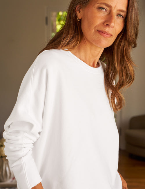 Woman wearing a white sweater indoors with a neutral background, view 3