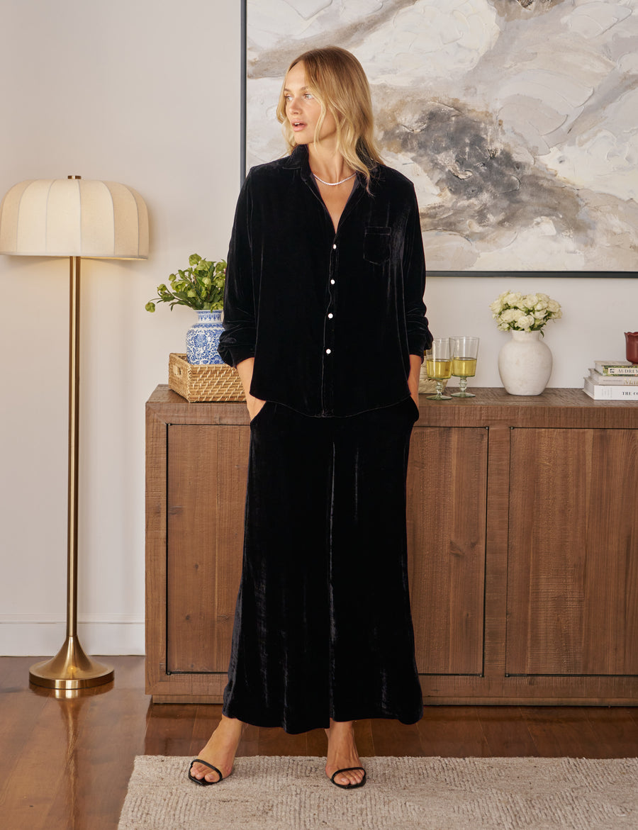Woman in a black velvet outfit standing in a stylish room with decor elements.