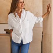 Woman wearing a white shirt and blue jeans standing in a room with wooden walls.