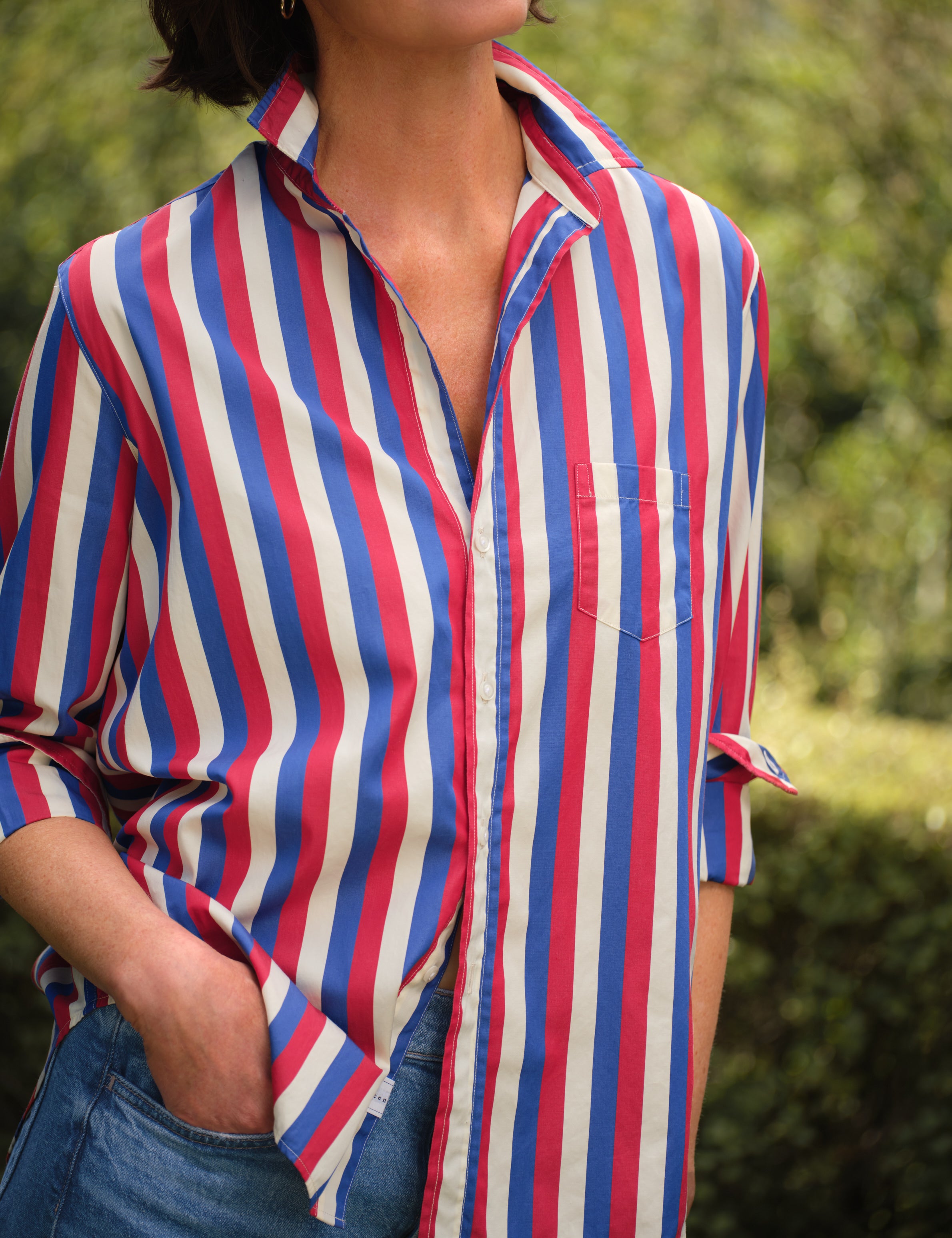 Person wearing a red, white, and blue striped shirt with a blurred natural background, view 5