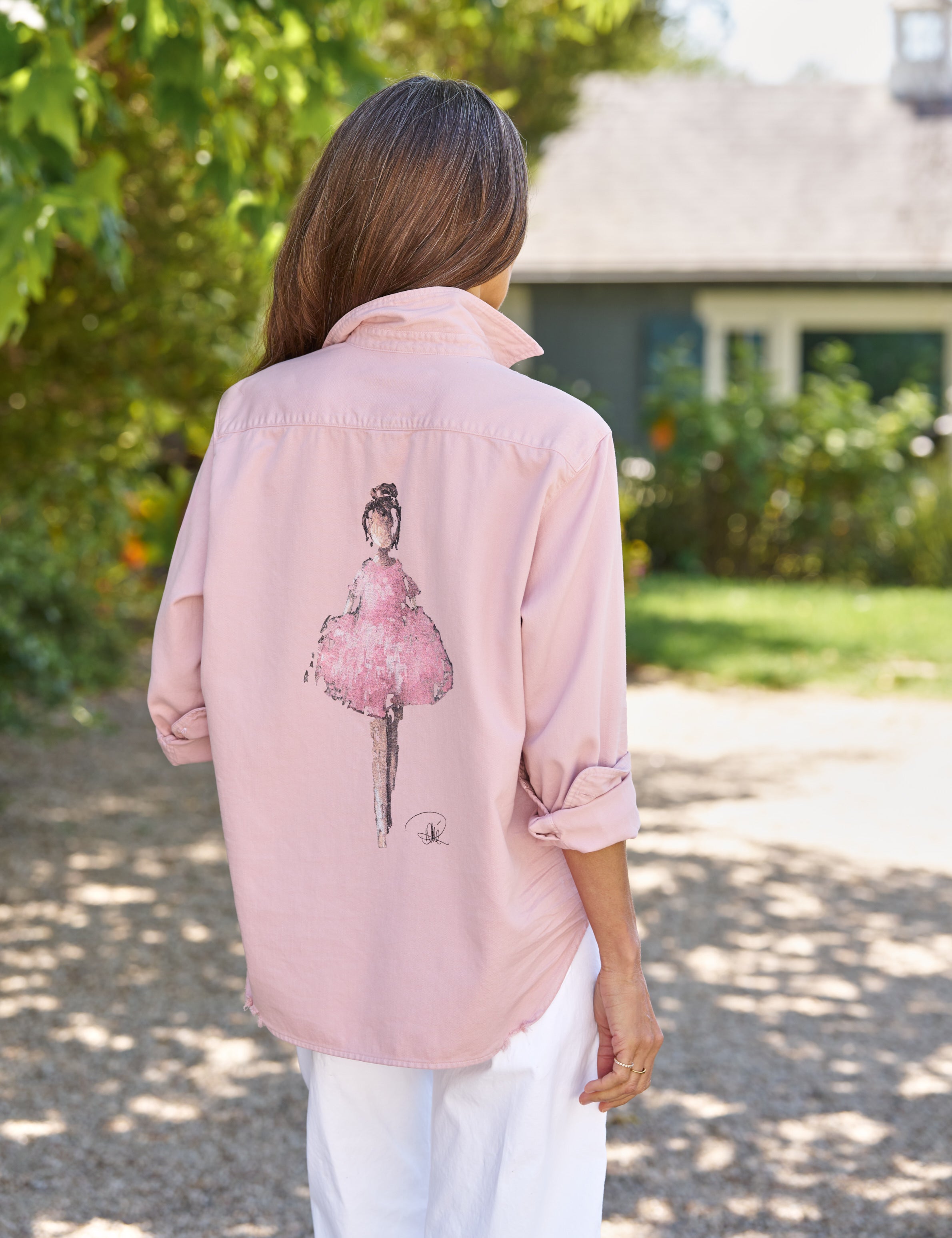 Person wearing a pink shirt with a graphic of a ballerina outdoors., front view