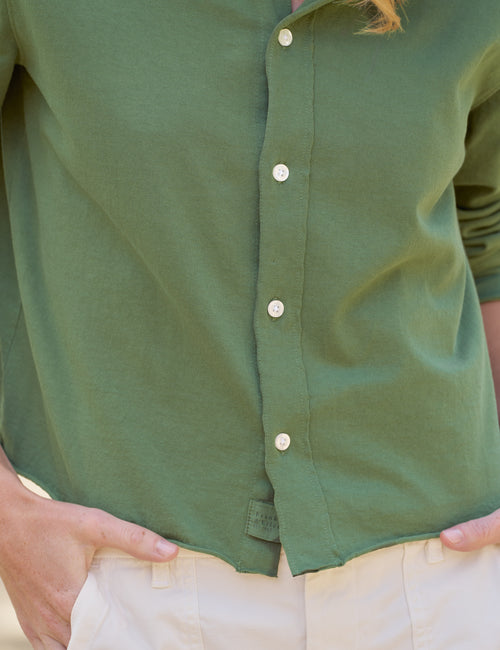 Close-up of a person wearing an olive green button-up shirt tucked into light beige pants, with hands in pockets., view 3