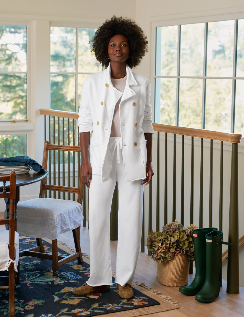 Person wearing a white outfit standing in a room with large windows and green boots on the floor.