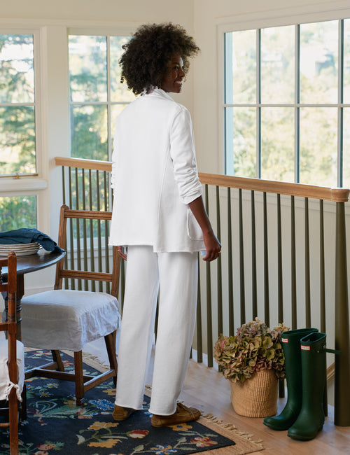 Person wearing a white outfit standing in a room with large windows and green boots., alternate view