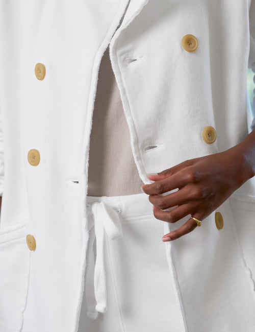 White coat with light brown buttons worn by a person, with a focus on the coat's details., view 3