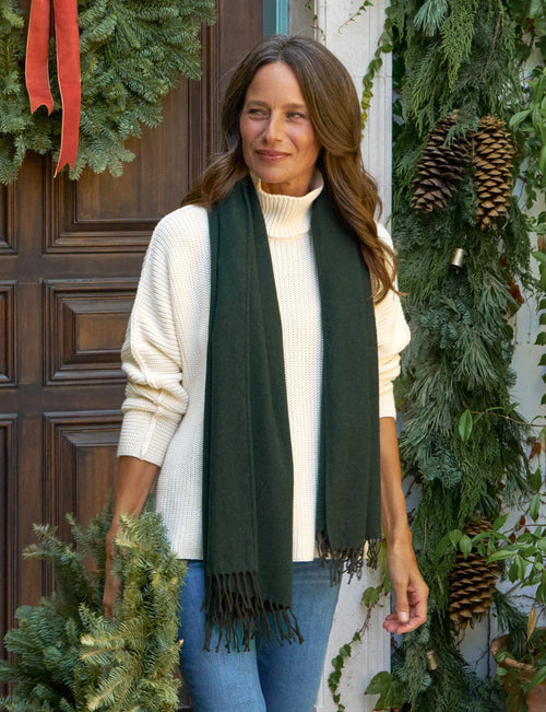 Woman holding a wreath in front of a door decorated with greenery and a red ribbon., front view