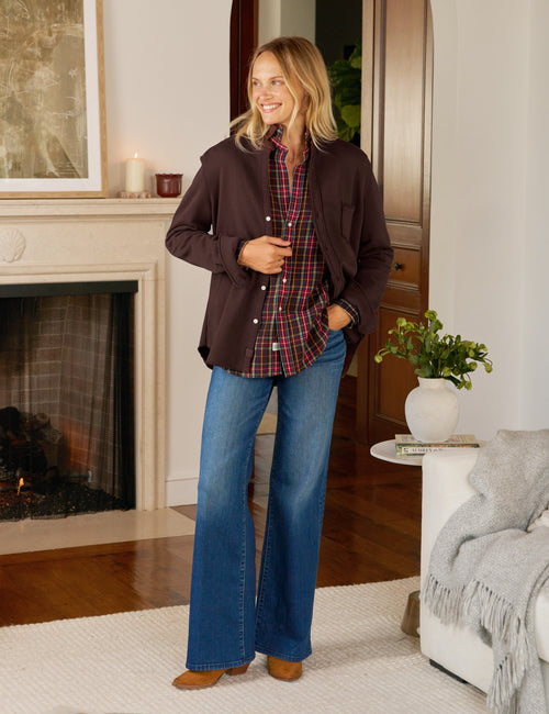 Woman standing in a living room wearing a brown jacket, plaid shirt, and blue jeans., view 5