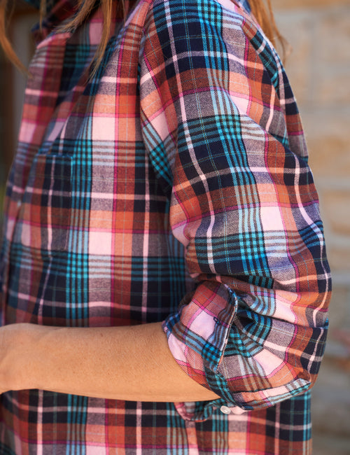 A close-up of a person wearing a long-sleeve plaid flannel shirt with rolled-up sleeves, showing a multicolor pattern of pink, orange, blue, and navy., view 3