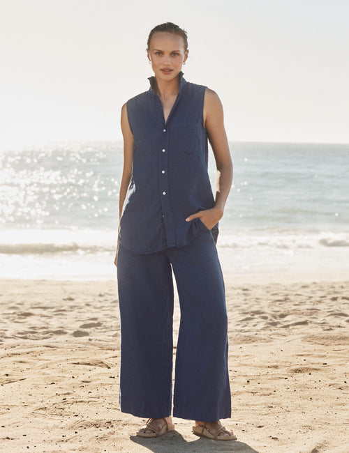 Woman in navy sleeveless top and wide-leg pants standing on a beach., front view
