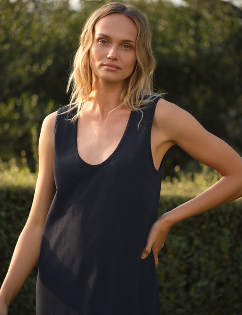 Woman wearing a navy sleeveless dress outdoors with greenery in the background, view 3