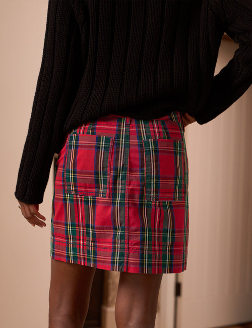 A model wearing a red tartan plaid mini skirt with green, yellow, and blue stripes, paired with a black ribbed knit sweater., alternate view