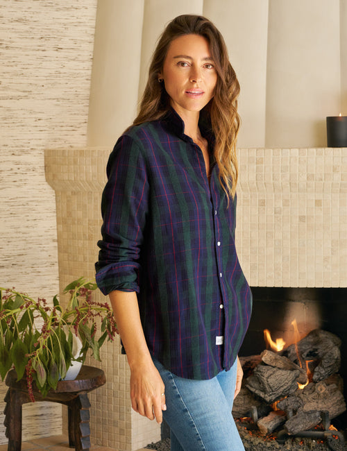 Woman wearing a plaid shirt standing in front of a fireplace, front view