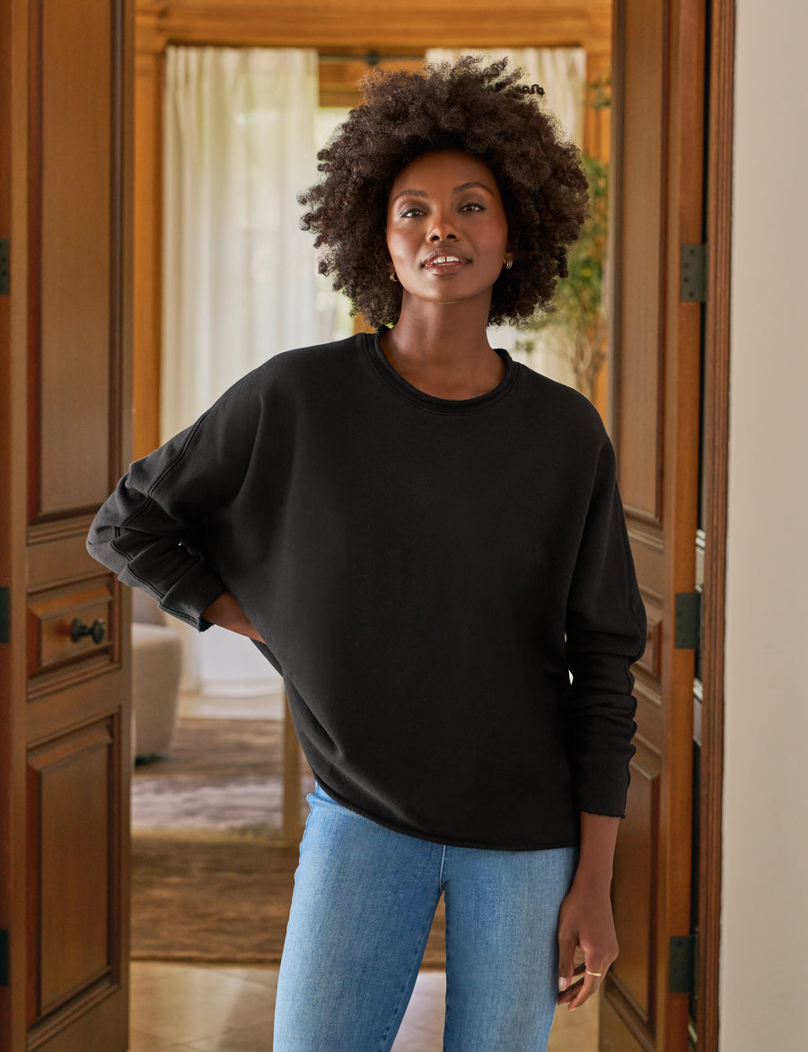 Woman wearing a black sweater and blue jeans standing in a doorway.